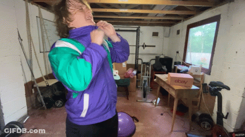 A Man In A Purple And Green Jacket Is Standing In A Garage With A Box That Says Ebay GIF