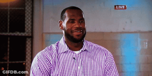 A Man In A Purple And White Checkered Shirt Is Smiling In Front Of A Live Sign GIF
