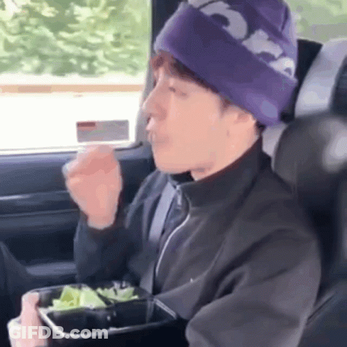 A Man In A Purple Hat Is Sitting In The Back Seat Of A Car Eating A Salad . GIF