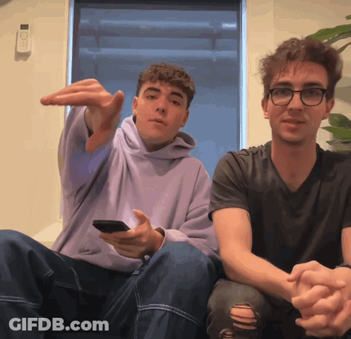A Man In A Purple Hoodie Is Sitting Next To A Man In A Black Shirt GIF