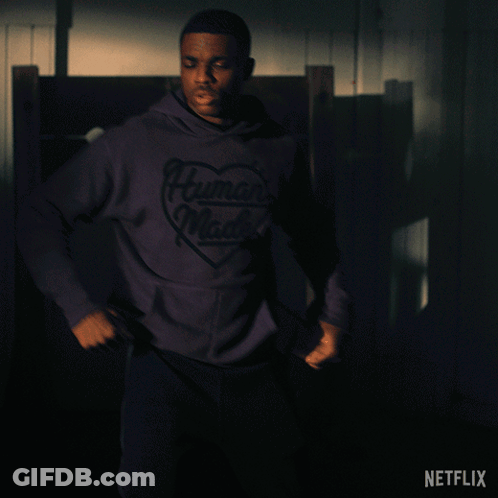 A Man In A Purple Human Made Hoodie Stands In A Dark Room GIF