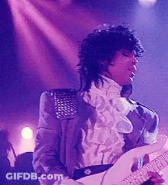 A Man In A Purple Jacket And White Shirt Is Playing A Guitar On Stage . GIF