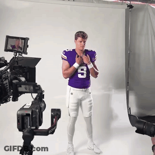 A Man In A Purple Jersey With The Number 3 On It Stands In Front Of A Camera GIF