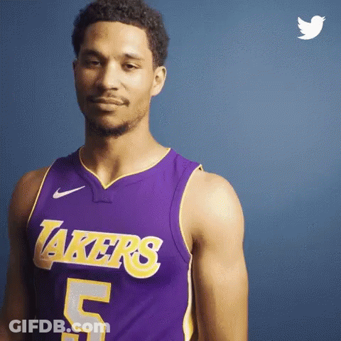 A Man In A Purple Lakers Jersey Is Standing In Front Of A Blue Wall . GIF