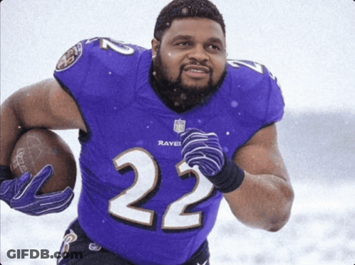 A Man In A Purple Ravens Jersey Holds A Football GIF