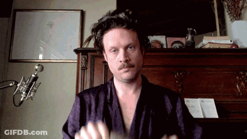 A Man In A Purple Robe Stands In Front Of A Microphone In A Room GIF