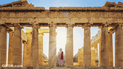 A Man In A Purple Robe Stands In Front Of A Row Of Columns With The Sun Shining Through Them GIF