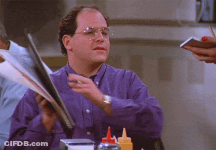 A Man In A Purple Shirt And Glasses Is Holding A Menu GIF