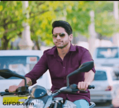 A Man In A Purple Shirt And Sunglasses Is Riding A Motorcycle GIF