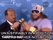 A Man In A Purple Shirt And Sunglasses Is Talking Into A Microphone While Another Man Looks On . GIF