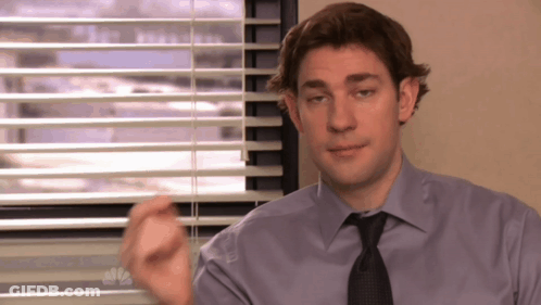 A Man In A Purple Shirt And Tie Is Sitting In Front Of A Window With Blinds GIF
