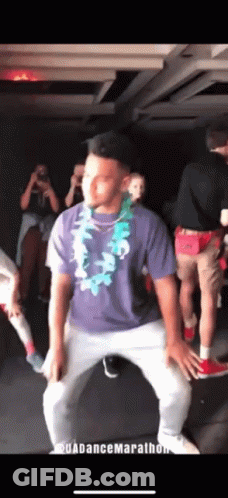 A Man In A Purple Shirt And White Pants Is Dancing In A Dark Room GIF