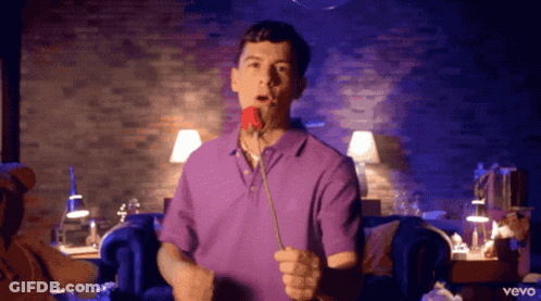 A Man In A Purple Shirt Holds A Rose In His Mouth GIF