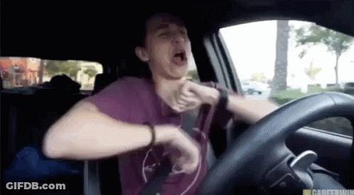 A Man In A Purple Shirt Is Driving A Car And Yawning GIF