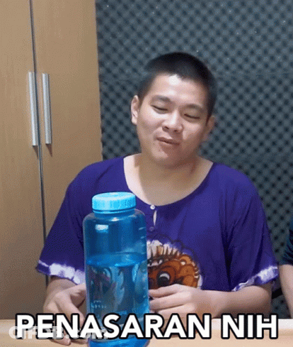A Man In A Purple Shirt Is Holding A Blue Water Bottle With The Words Penasaran Nih Written On It GIF