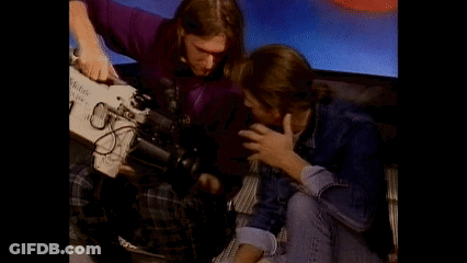 A Man In A Purple Shirt Is Holding A Camera That Says Kodak On It GIF