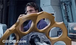 A Man In A Purple Shirt Is Looking At A Large Gold Object In A Room . GIF