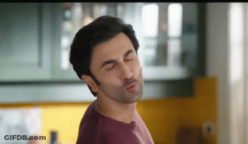 A Man In A Purple Shirt Is Making A Funny Face With His Eyes Closed . GIF