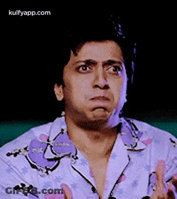 A Man In A Purple Shirt Is Making A Funny Face With His Hands . GIF