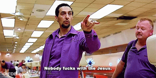 A Man In A Purple Shirt Is Pointing At Another Man In A Bowling Alley While Talking . GIF