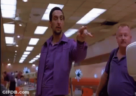 A Man In A Purple Shirt Is Pointing At Someone In A Bowling Alley GIF