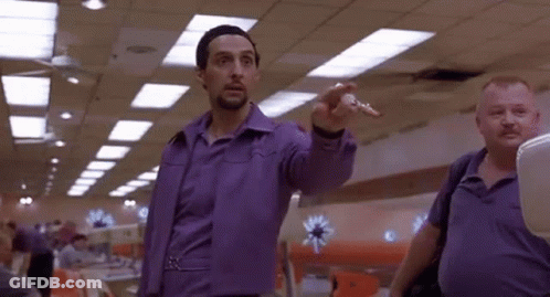A Man In A Purple Shirt Is Pointing At Something While Standing Next To Another Man . GIF