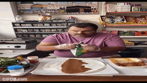 A Man In A Purple Shirt Is Sitting At A Table With A Tortilla On It GIF
