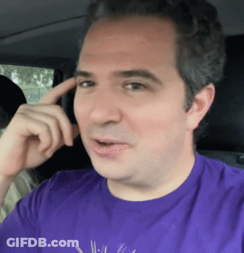 A Man In A Purple Shirt Is Sitting In A Car With His Finger On His Forehead GIF