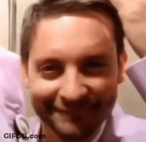 A Man In A Purple Shirt Is Smiling For The Camera . GIF