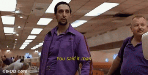 A Man In A Purple Shirt Is Standing Next To Another Man In A Bowling Alley . GIF
