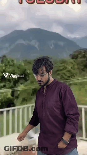 A Man In A Purple Shirt Is Standing On A Balcony With A Mountain In The Background GIF