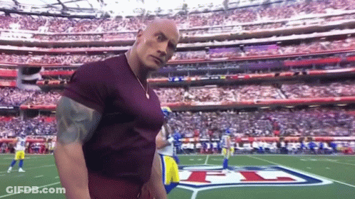 A Man In A Purple Shirt Is Standing On A Football Field In Front Of A Stadium Full Of People . GIF