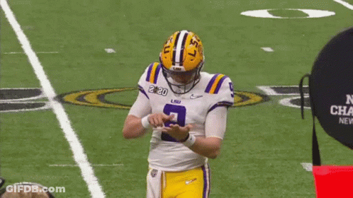 A Man In A Purple Shirt Is Talking To A Football Player In A Lsu Uniform . GIF