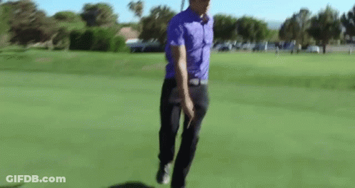 A Man In A Purple Shirt Is Walking On A Golf Course . GIF