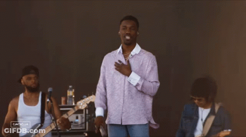 A Man In A Purple Shirt Sings Into A Microphone While Another Man Plays Guitar GIF
