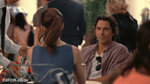 A Man In A Purple Shirt Sits At A Table Talking To A Woman GIF
