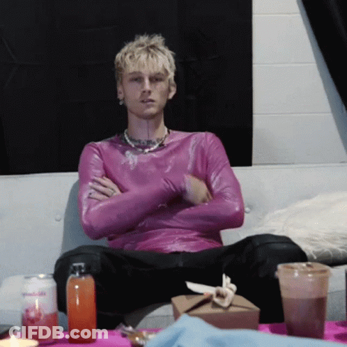 A Man In A Purple Shirt Sits On A Couch With His Arms Crossed GIF
