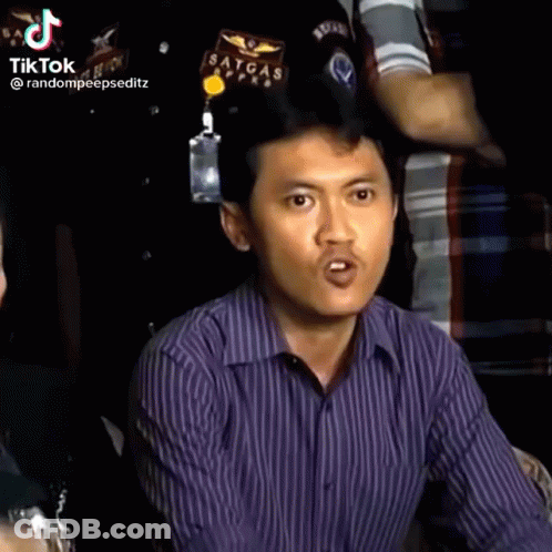 A Man In A Purple Striped Shirt Is Making A Funny Face While Sitting In A Crowd . GIF