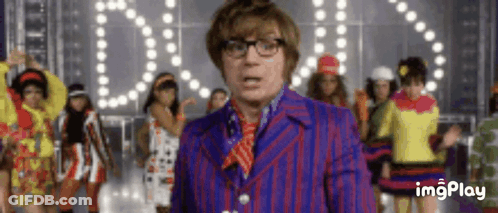 A Man In A Purple Suit And Red Tie Is Standing In Front Of A Group Of Women Dancing . GIF