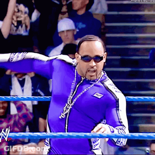 A Man In A Purple Suit And Sunglasses Stands In A Wrestling Ring With A Watermark That Says The Next Thing GIF