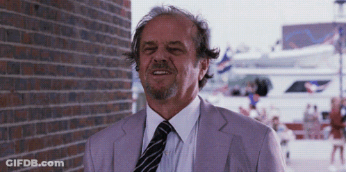 A Man In A Purple Suit And Tie Is Smiling In Front Of A Brick Wall GIF