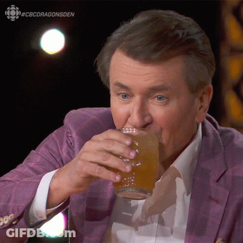 A Man In A Purple Suit Is Drinking From A Glass With #Cbcdragonsden Written On The Bottom GIF
