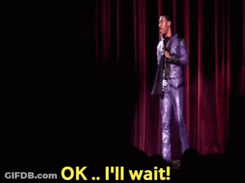 A Man In A Purple Suit Is Standing On A Stage Holding A Microphone And Saying Ok . GIF
