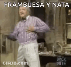 A Man In A Purple Sweater And White Pants Is Dancing In A Room With His Hands On His Chest . GIF