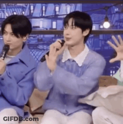 A Man In A Purple Sweater Is Holding A Microphone And Talking Into It . GIF