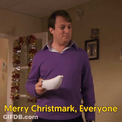 A Man In A Purple Sweater Is Holding A White Object And Says Merry Christmark Everyone GIF