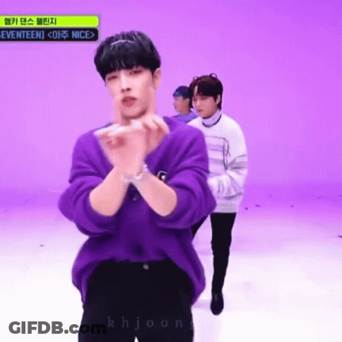 A Man In A Purple Sweater Is Standing In Front Of A Purple Wall . GIF