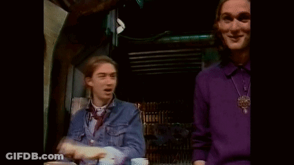 A Man In A Purple Sweater Is Waving At Another Man In A Blue Shirt . GIF