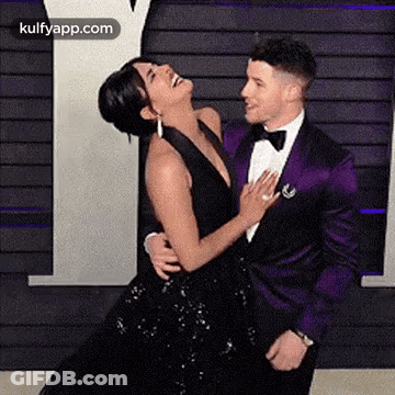 A Man In A Purple Tuxedo And A Woman In A Black Dress Are Dancing Together . GIF