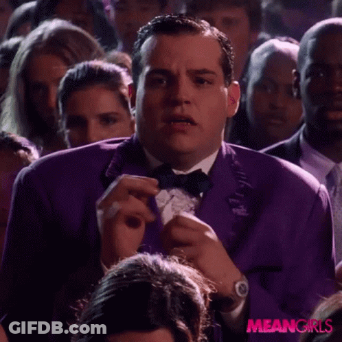 A Man In A Purple Tuxedo And Bow Tie Is In A Crowd Of People . GIF